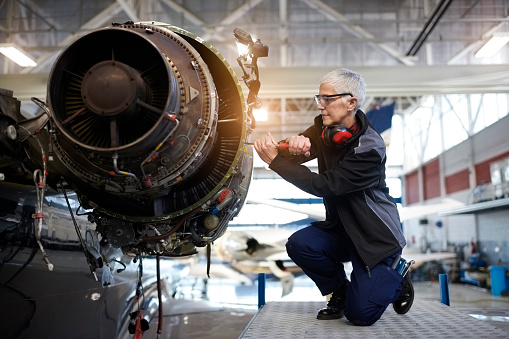 Senior female engineer in the hangar repairing and maintaining airplane jet engine.