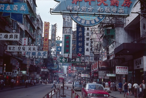 Hong Kong, China, 1977. Street scene in Hong Kong: characters, advertising, shops cars, buildings and pedestrians.