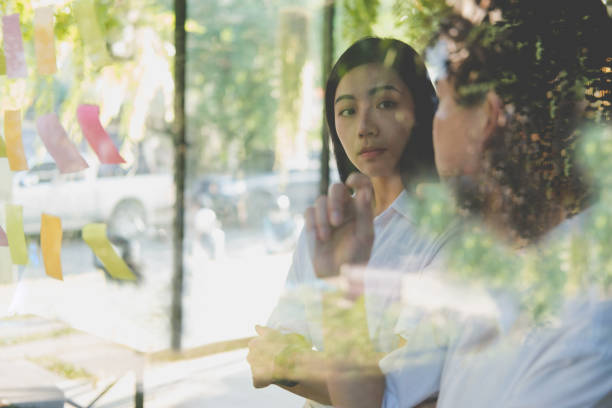 istock man & woman discussing creative idea with adhesive notes on glass wall at workplace. Sticky note paper reminder schedule at office. business, brainstorming, creativity concept 906895964