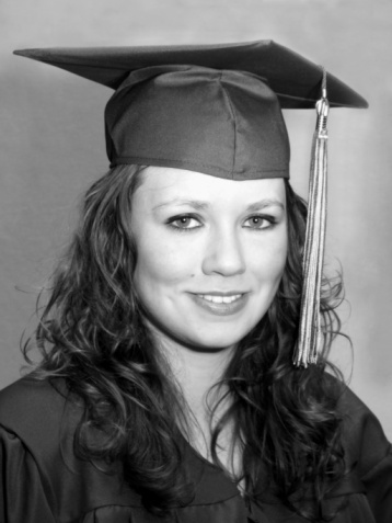 A young hispanic woman wearing a cap and gown. She is a first generation university or high school graduate, smiling at the camera.