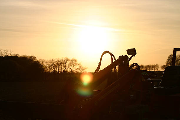 Silhouette Of Field Being Plowed By Agricultural Equipment Unfolds As The Sun Sets,Creating A Picturesque Scene Against The Fading Light