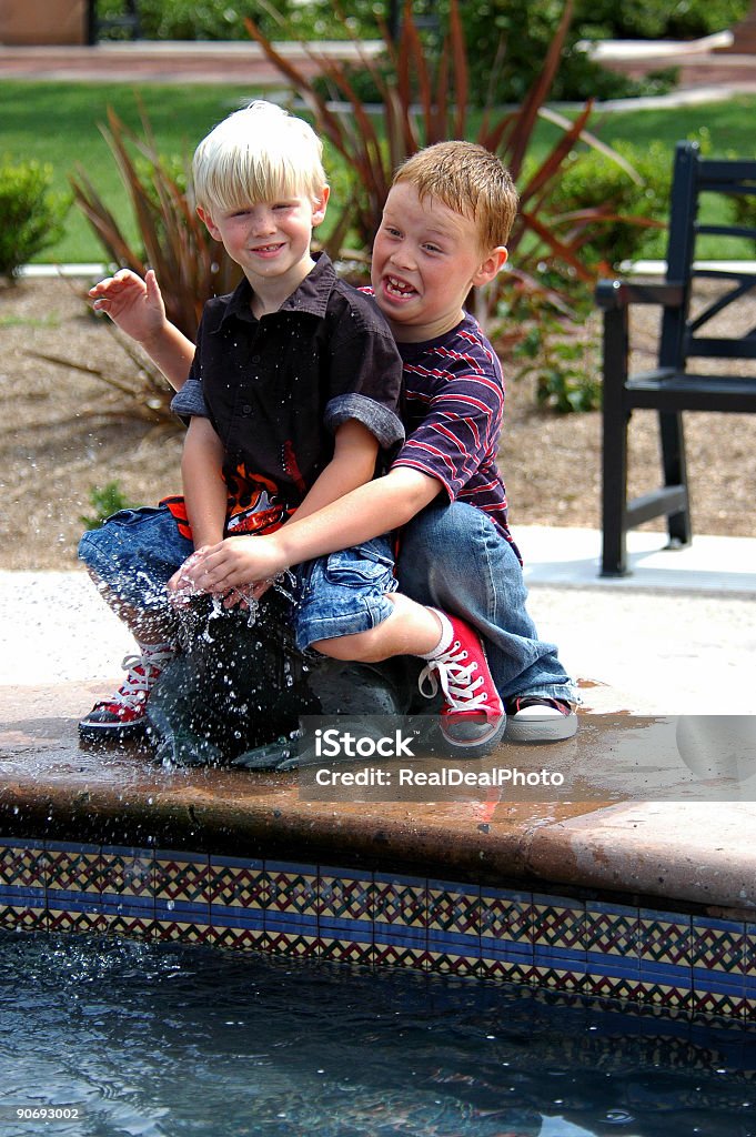 Brothers Brothers playing in the park fountian while his dad watches Blond Hair Stock Photo