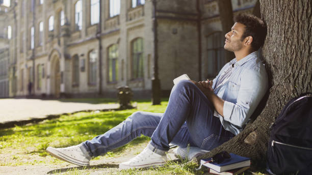 istock Dreamy young male sitting with notebook under tree, thinking what to write, idea 906951038