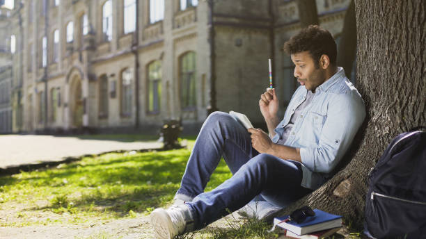 Mixed-race male sitting under tree, writing in sketchbook, innovative idea