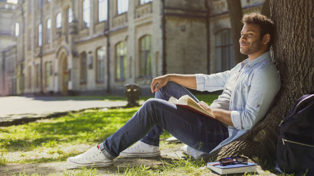 istock Multiracial guy sitting under tree, looking and smiling at somebody, friendly 906954812