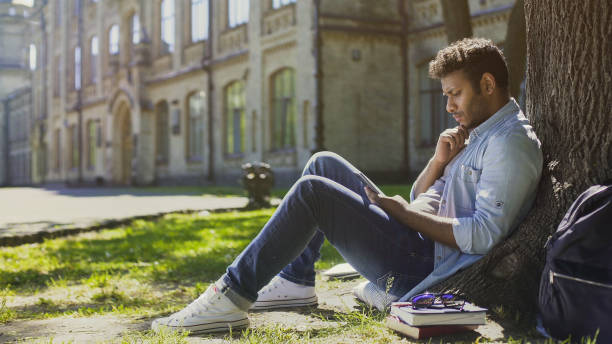 istock Male sitting under tree, using mobile phone, reacting to newsfeed, confusion 906959624