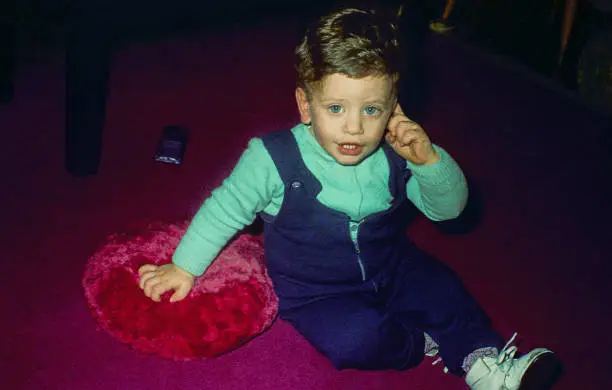 vintage  image of a cute kid looking from the seventies sitting on the floor and looking at camera.