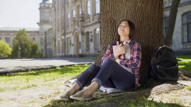 istock Mixed female reading book under tree, pressing it against chest, favorite book 906967366
