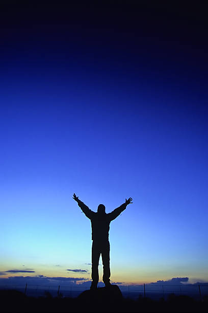 istock silhouette man arms raised into sunset sky landscape 90697166