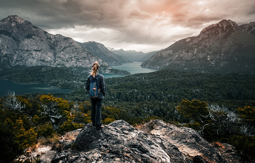 Woman hiker stands and enjoys valley view from viewpoint. Hiker reached top of the mountain and watching sunset. Patagonia, Argentina