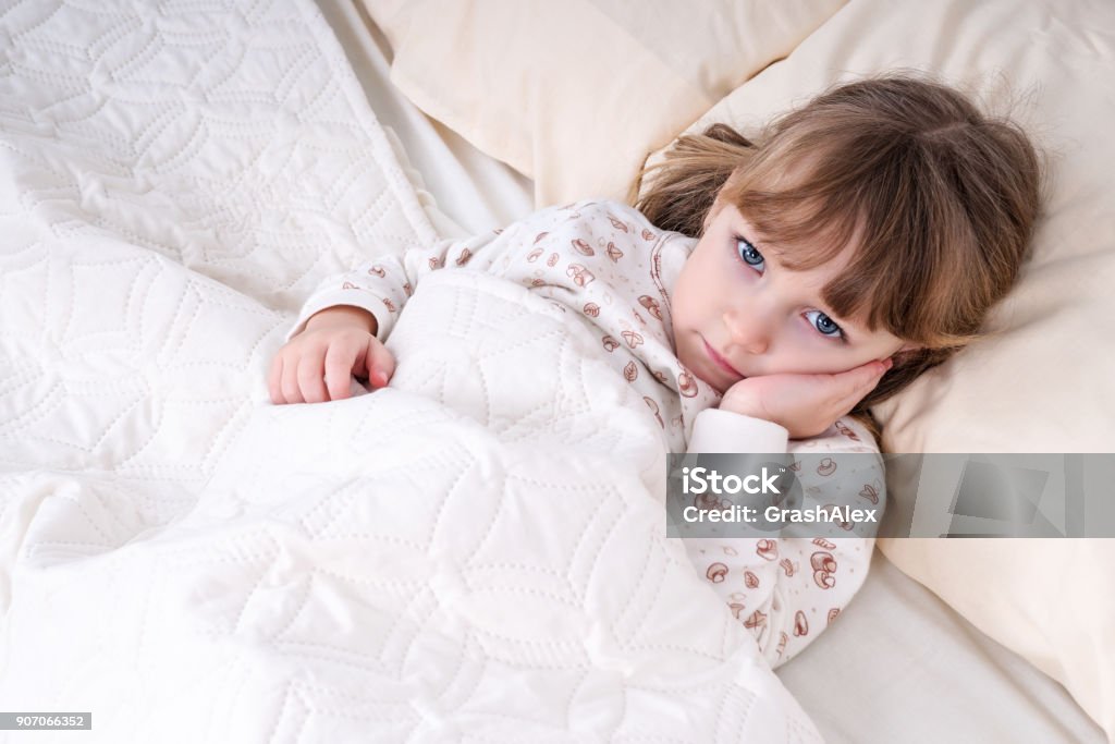 Child in bed with hand on cheek Little beautiful girl lying in bed and holding her cheek with a sick tooth Child Stock Photo