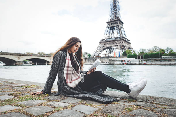 istock Young woman reading book on seine river coastline 907070790
