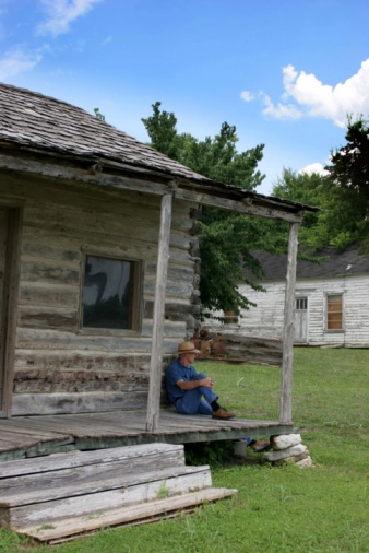 Man sitting on porch of an old cabin from the 1800's.
