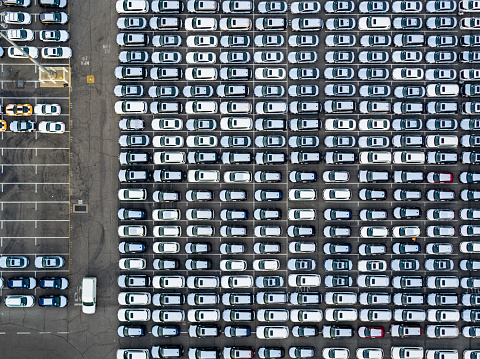 Scores of brand new cars wrapped in plastic, arranged in a grid, seen from above.