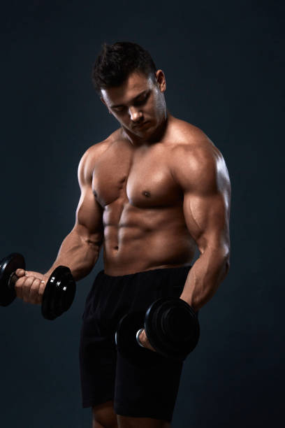 istock Muscular bodybuilder doing exercises with dumbbell over black background.Strong athletic man shows body,abdominal muscles,biceps and triceps.Work out,gaining weight,pumping up muscles with dumbbells. 907126956
