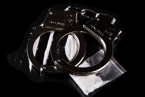 Handcuffs and cocaine on black background