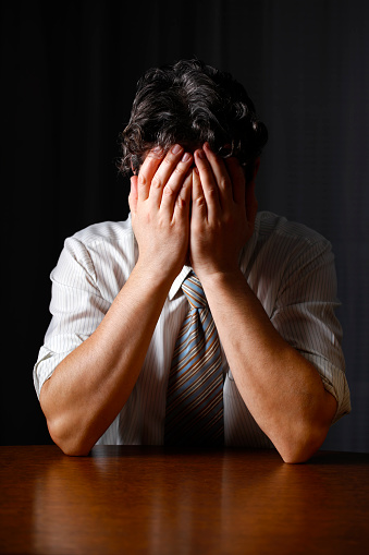 Depressed businessman covering face with his hands. Space for copy on the desk.