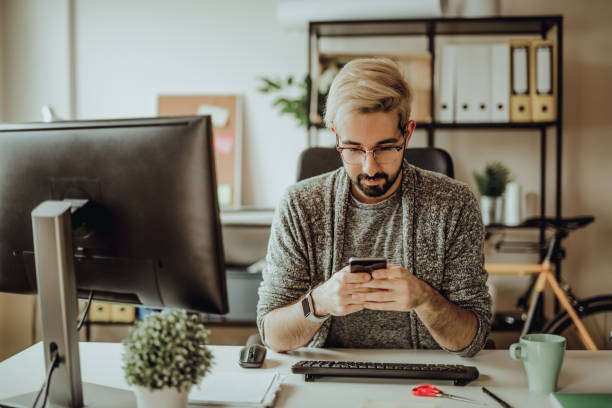 istock Young hipster typing a message on his smartphone in the office during morning hours 907180564