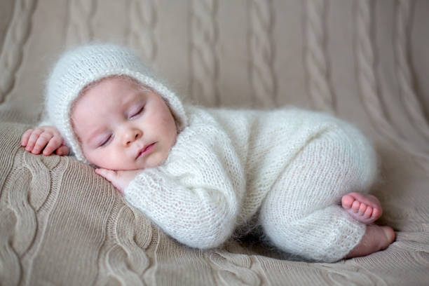 istock Beatiful baby boy in white knitted cloths and hat, sleeping 907221762