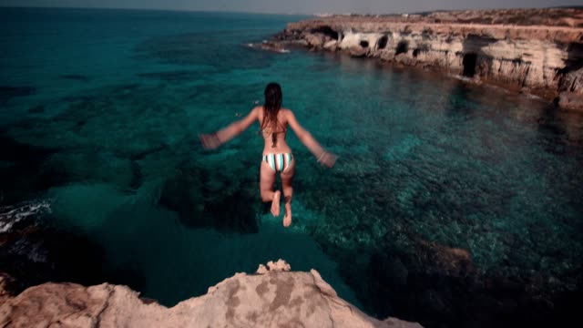 Young woman jumping into ocean from rock cliff