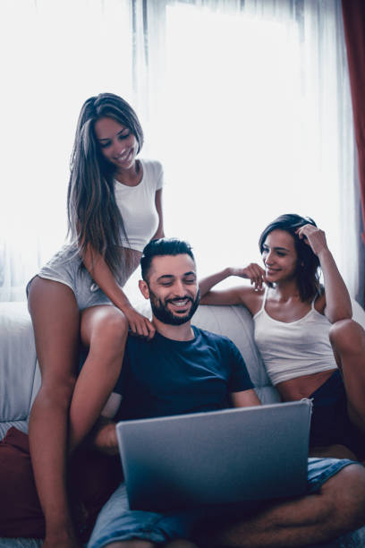 istock Smiling Friends Sitting on Sofa and Making Video Conference on Laptop 907291044