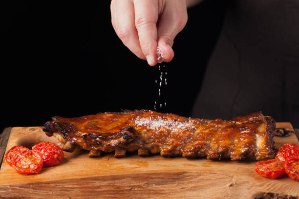 el chef rocía sal listos para comer costillas de cerdo, en una vieja mesa de madera. un hombre prepara un bocadillo de cerveza sobre un fondo negro con espacio de copia - sweet chili fotografías e imágenes de stock