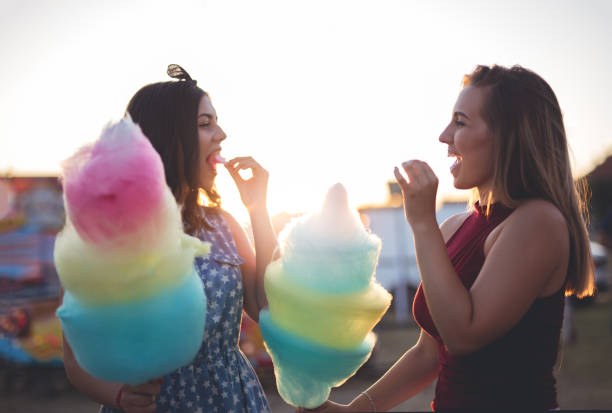 istock Two girls eating candyfloss at amusement park 907306208