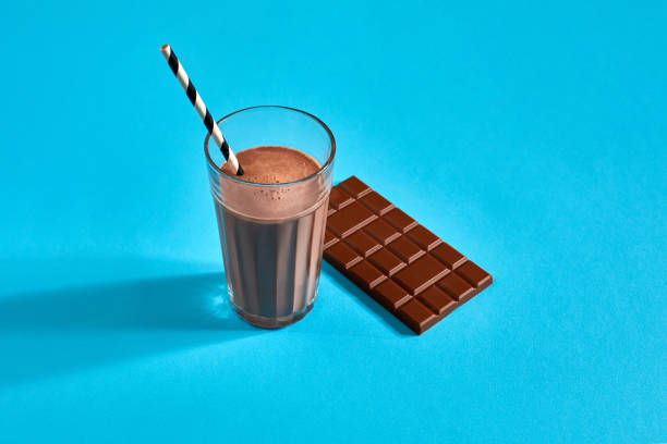 bicchiere di latte al cioccolato con barretta di cioccolato su sfondo blu con spazio per testo o design - biscuit cookie cake variation foto e immagini stock