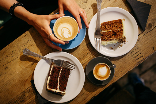 Vintage low key image of a coffee on the table in a cafe in East London. Young woman is having a cappuccino and some sweets, a delicious carrot cake and some chocolate brownie.