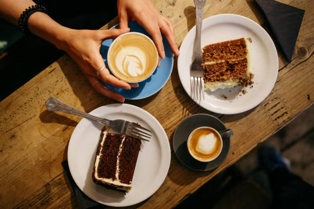 Coffee and cake on the table in a cafe in East London Vintage low key image of a coffee on the table in a cafe in East London. Young woman is having a cappuccino and some sweets, a delicious carrot cake and some chocolate brownie. cake stock pictures, royalty-free photos & images