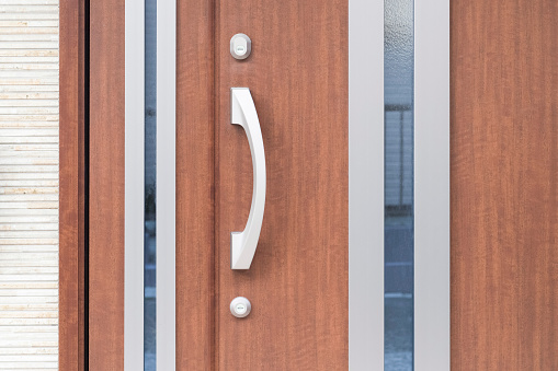 Close-up on the letterbox and door handle on a wood and glass front door, taken from the exterior.