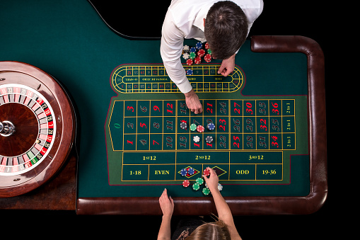 Man croupier and woman playing roulette at the table in the casino. Top view at a roulette green table with a tape measure. Table for gambling in a luxury casino. Gambling. Casino roulette