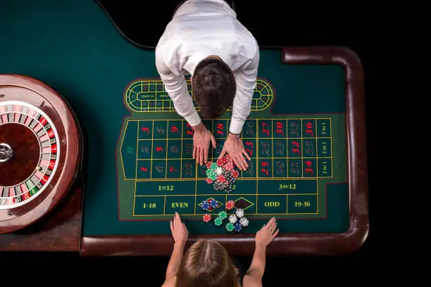 Photo of Man croupier and woman playing roulette at the table in the casino. Top view at a roulette green table with a tape measure