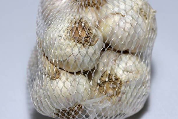 istock White garlic in the white plastic net isolated on light grey background. 907428116