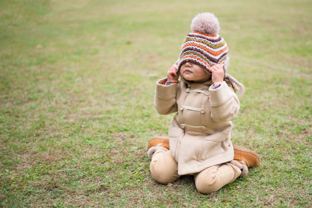 Portrait of preschooler boy wearing a fashionable coat, hat and scarf in outdoor. He is sitting in front of an old antique wooden door.