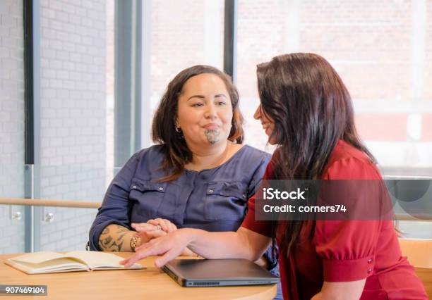 Foto de Maori E Mulheres De Negócios Caucasiano Sorrindo Na Reunião Pode Ser Administração Funcionários Ou Colegas De Trabalho Fêmea Maori Tem Uma Tatuagem Facial Moko e mais fotos de stock de Espontânea