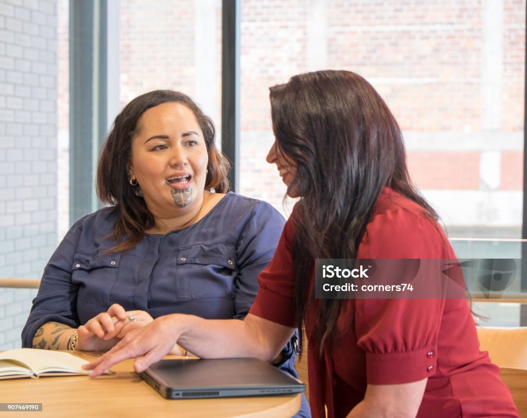 Maori and caucasian business women talking in meeting, could be coworkers, employees or management. Maori female has moko facial tattoo. Maori and caucasian business women talking in meeting, could be coworkers, employees or management. Maori female has moko facial tattoo. Photographed in New Zealand, NZ Discussion Stock Photo