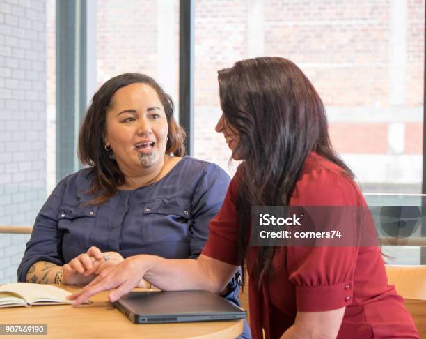 Maori And Caucasian Business Women Talking In Meeting Could Be Coworkers Employees Or Management Maori Female Has Moko Facial Tattoo Stock Photo - Download Image Now