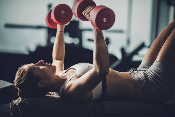 istock Female athlete having chest exercise with dumbbells in a gym. 907487926