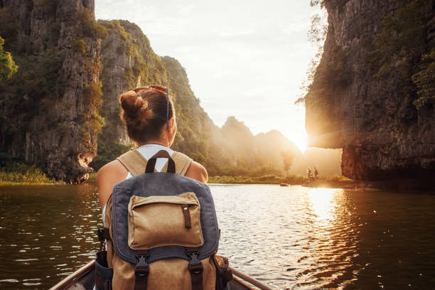 woman with backpack traveling by boat enjoying sunset among of mountains. stock photo
