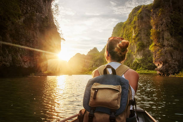 Woman traveling by boat enjoying sunset among of karst mountains Happy woman with backpack traveling by boat enjoying sunset among of karst mountains in the North of Vietnam. river swimming women water stock pictures, royalty-free photos & images