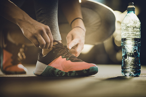 Close up of unrecognizable female athlete tying shoelaces on her sneakers.