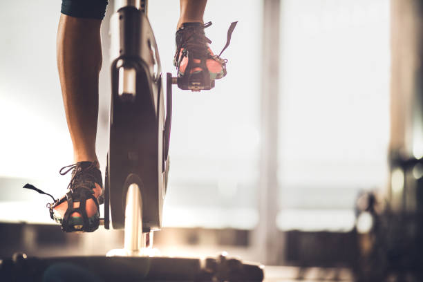 Unrecognizable female athlete exercising on exercise bike in a gym. Unrecognizable athletic legs during exercising training in a health club. spin bike stock pictures, royalty-free photos & images