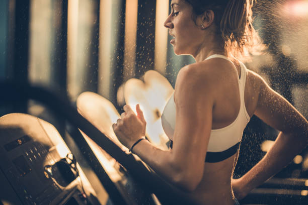 汗をかいた女性スポーツ ジムでトレーニング中にトレッドミルで実行されています。 - treadmill gym health club exercising ストックフォトと画像