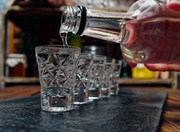 Vodka shots Crystal shot glasses of vodka standing in a row. Pouring vodka from a bottle to the shot glass shot glass stock pictures, royalty-free photos & images