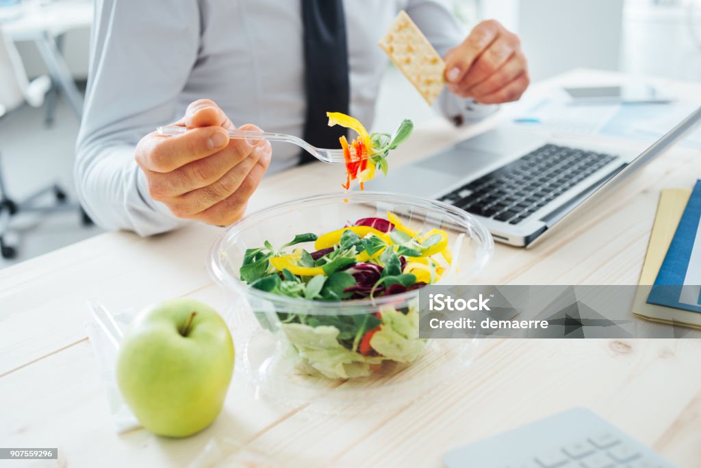 Businessman having a lunch break Businessman having a lunch break at desk, he is eating fresh salad and holding a cracker, unrecognizable person Office Stock Photo