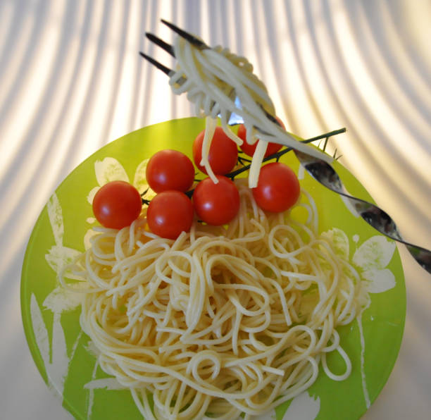 boiled spaghetti on a green plate with tomatoes and basil