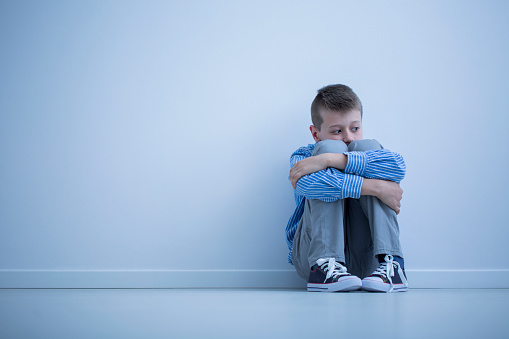Young boy with hypersensitivity sitting alone on the floor against the wall with copy space