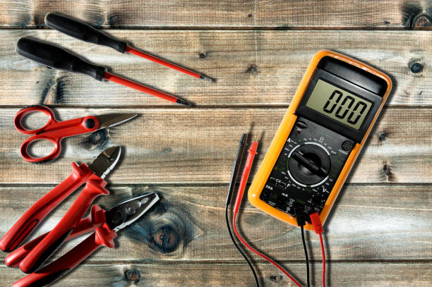 Close up from above of work tools on electrical installations, on an antique wooden table. Multimeter, clamp, cable cutter, scissors and screwdrivers for working on a residential electrical system photographed on an antique wooden desk. cable tester stock pictures, royalty-free photos & images