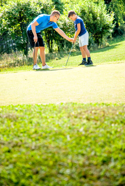 istock Golf Player Teaching a Child How to Hold the Golf Club for Teeing Off 907564010